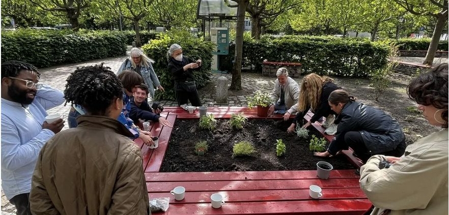 Das Bild zeigt Menschen, die um ein Kräuterbeet herum stehen und Kräuter einpflanzen.